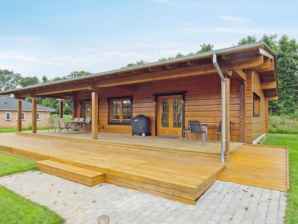 A wooden cabin with a covered porch, outdoor seating, and a barbecue grill.