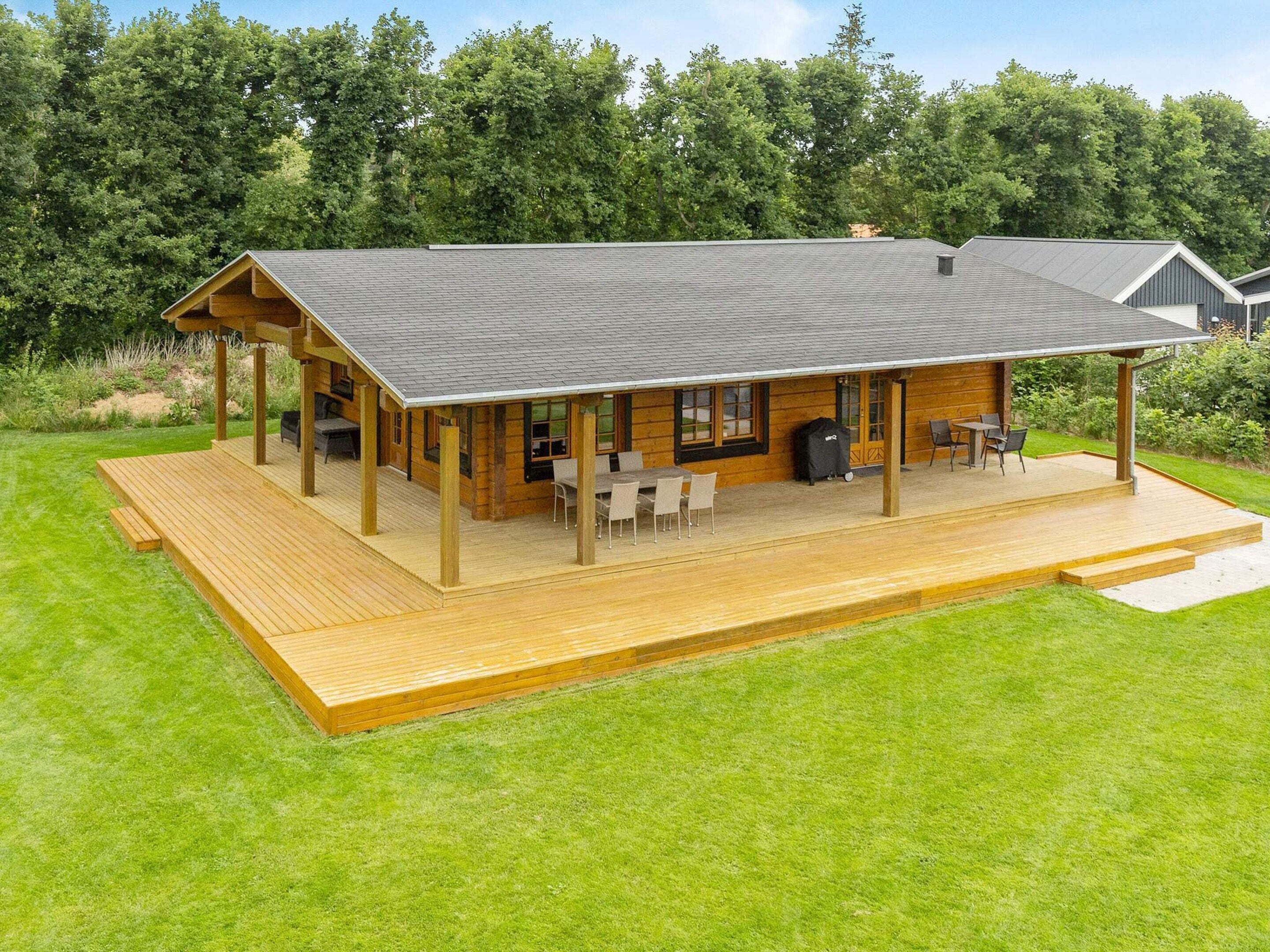 Eine Holzhütte mit überdachter Veranda, Sitzgelegenheiten im Freien und Grillplatz.