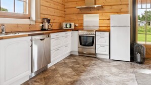 A compact kitchen with wooden walls, a stainless steel range, a microwave, and a white refrigerator.