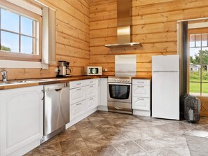 A compact kitchen with wooden walls, a stainless steel range, a microwave, and a white refrigerator.