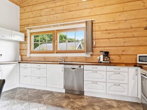 A modern kitchen with white cabinetry, a stainless steel dishwasher, and a window with curtains.