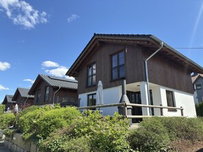 A two-story wooden house with a balcony, a chimney, and a garden in front. - Chalets am Diemelsee in Heringhausen (Diemelsee)