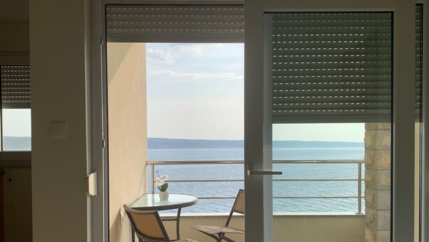 En balkon med bord og stole, havudsigt og en stenvæg.