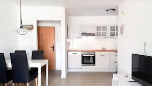 Une cuisine moderne avec des meubles blancs, un four encastré et un coin repas comprenant une table blanche et des chaises noires.