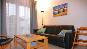 Un salon avec un canapé, une table basse en bois et un fauteuil. Il y a un tableau au mur et une lampe.
