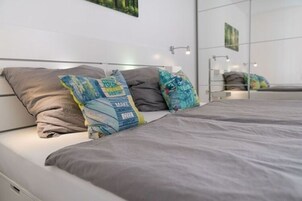 Ein modernes Schlafzimmer mit einem Bett, grauer Bettwäsche und dekorativen Kissen.