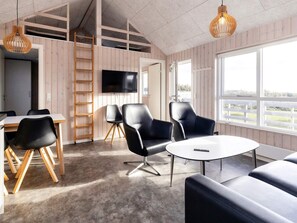 A modern interior with a wooden floor, a round table, and black leather chairs. There is a TV mounted on the wall and a ladder leaning against the wall. - 5 Star Holiday Home in Lokken (Lokken)
