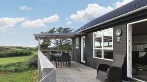 Una terraza de madera con mobiliario exterior, un ventanal y vistas al paisaje.