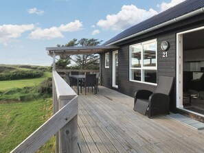 A wooden deck with outdoor furniture, a large window, and a view of the landscape. - 5 Star Holiday Home in Lokken (Lokken)