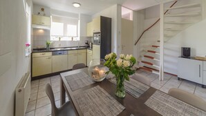 A modern kitchen with light-colored cabinets, a dining area with a table set for two, and a staircase leading to an upper floor. - Spacious Holiday Home With Sauna Near Beach (Wemeldinge)