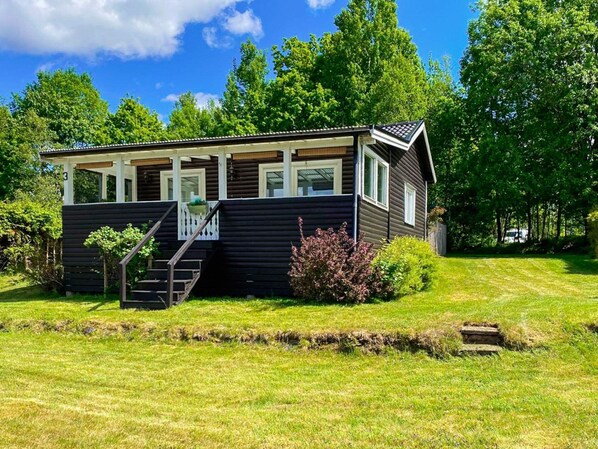 A small, single-story cabin with a porch, a staircase leading to the entrance, and a well-maintained lawn. - 4 Star Holiday Home in Boras (Borås)