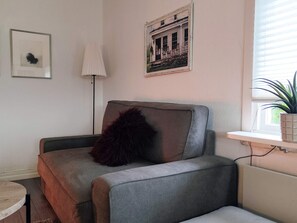 A living room with a grey sofa, a black cushion, a framed picture, a floor lamp, and a window with a plant. - 4 Star Holiday Home in Boras (Borås)