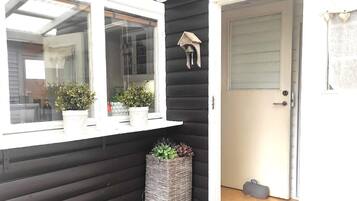 Fachada de madera oscura con un ventanal de marco blanco, una puerta y una pequeña campana en la pared.