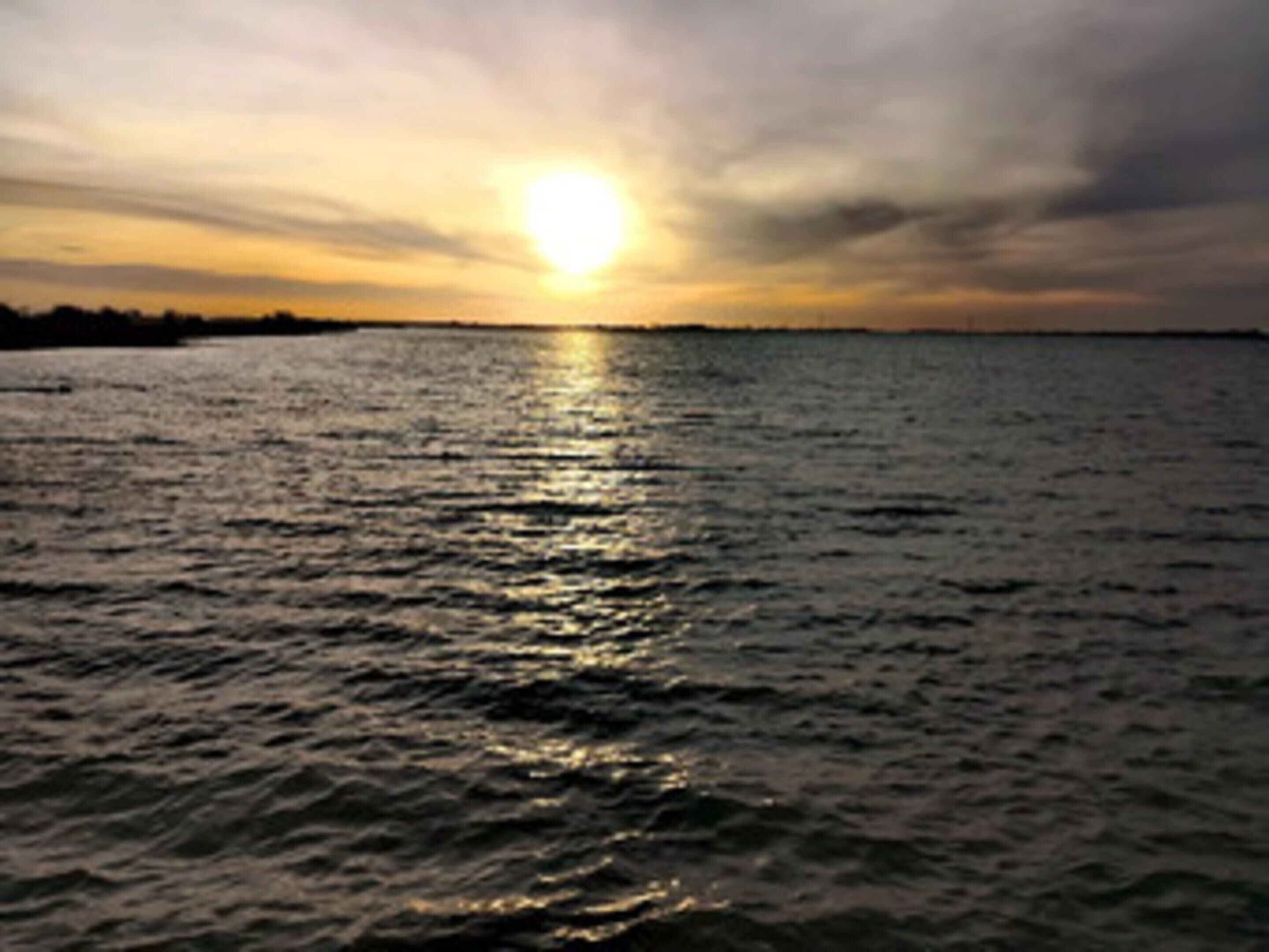 Un atardecer sobre un cuerpo de agua con una superficie tranquila que refleja el cielo.
