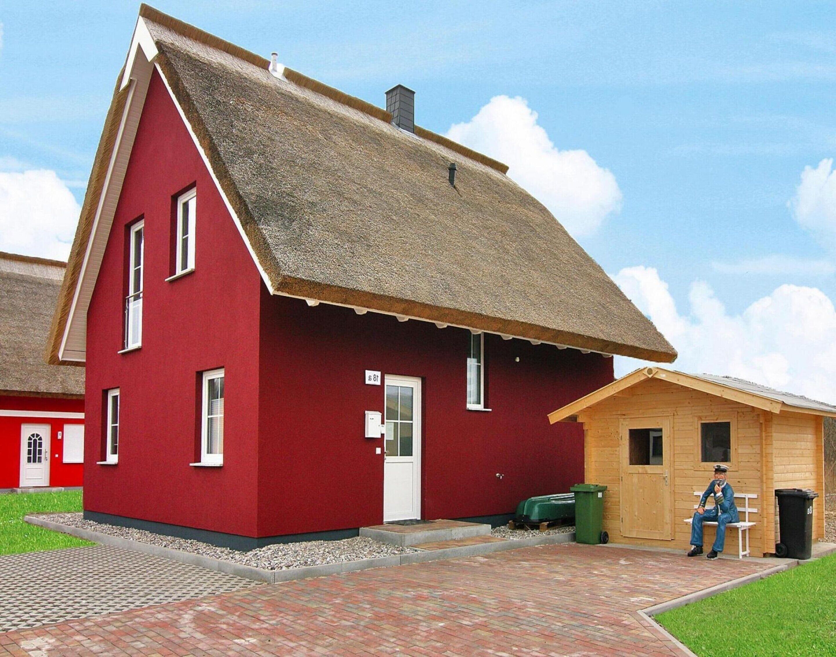 A red building with a thatched roof, a wooden door, and a small porch area.