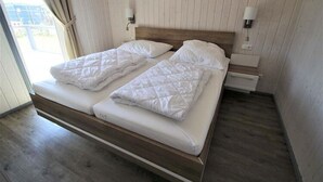 En dobbeltseng med trægavle og hvidt sengetøj, to sengeborde med lamper, samt udsigt til det fri gennem et vindue.