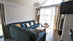 En moderne stue med en hjørnesofa, et sofabord, et fjernsyn og udsigt gennem en glasdør.
