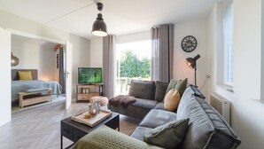 A modern living room with a sofa, a coffee table, a TV, and a balcony with curtains. - Holiday Home in Quiet Park With Garden (Wemeldinge)