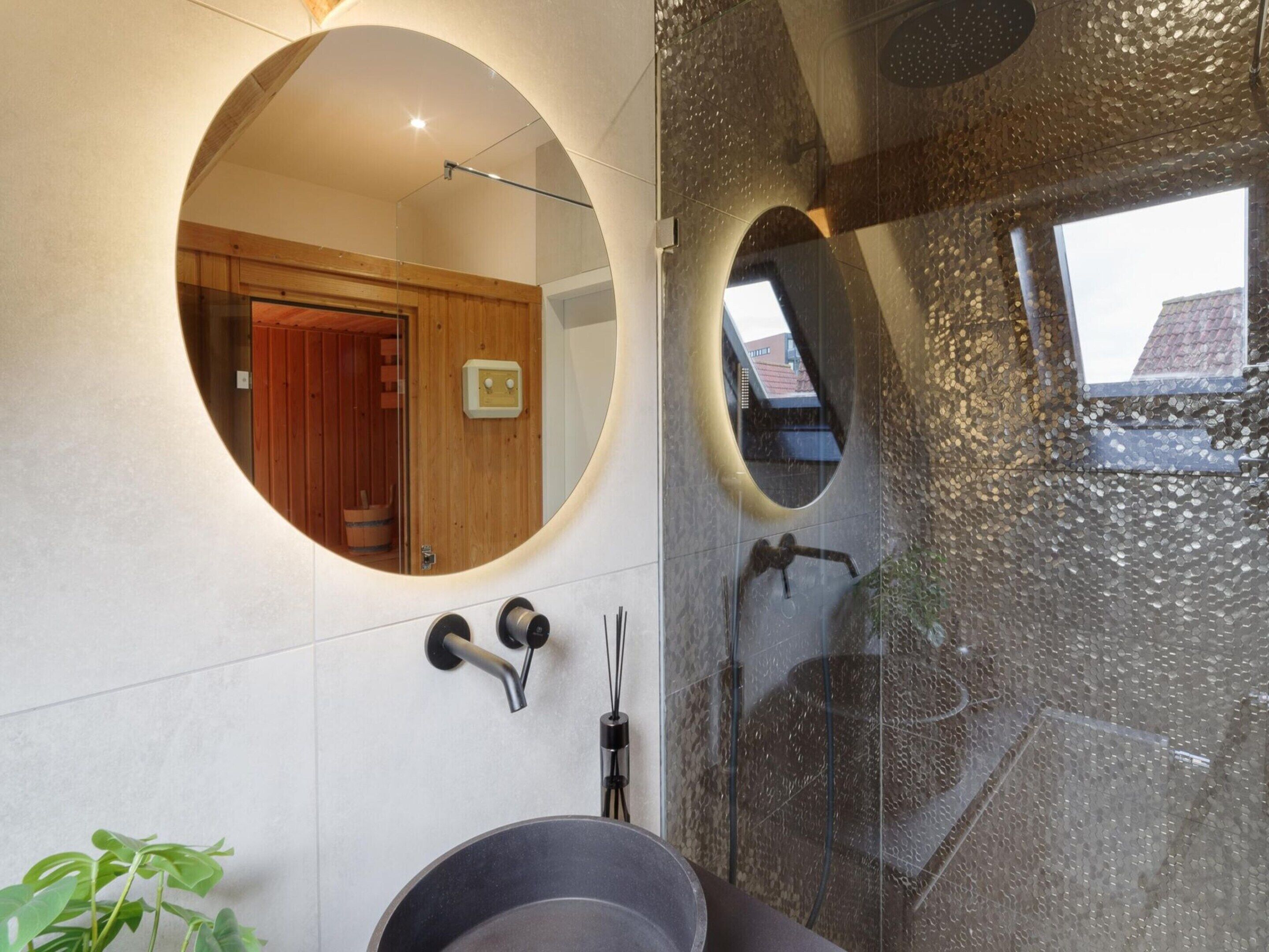 A modern bathroom with a circular mirror, a shower area, and a visible wooden door.