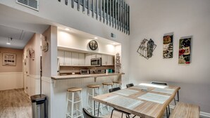 Een moderne keuken met witte kastjes, een centraal eiland met krukken, een magnetron en een klok aan de muur.