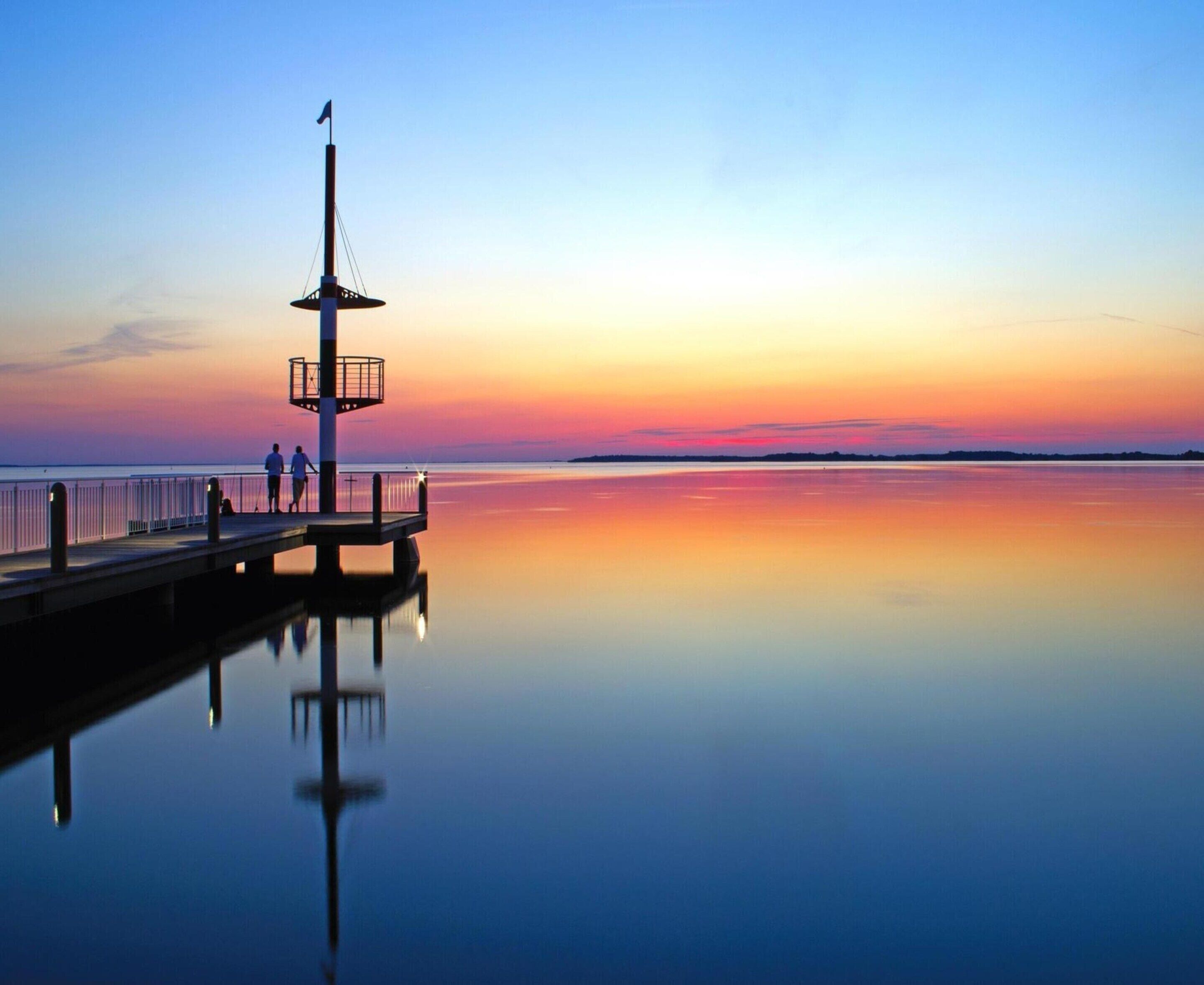 Een steiger die uitsteekt in kalm water, met een heldere lucht tijdens de zonsondergang.