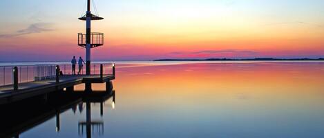 A pier extending into calm waters with a clear sky at sunset.