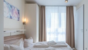 Una habitación de hotel con una cama grande, una mesita de noche, una lámpara de pared y una ventana con cortinas.