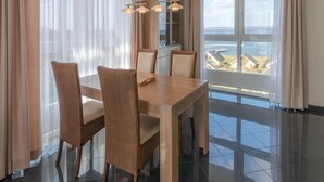 Un comedor moderno con una mesa de madera y sillas de mimbre, ventanas amplias con cortinas y vista al mar.