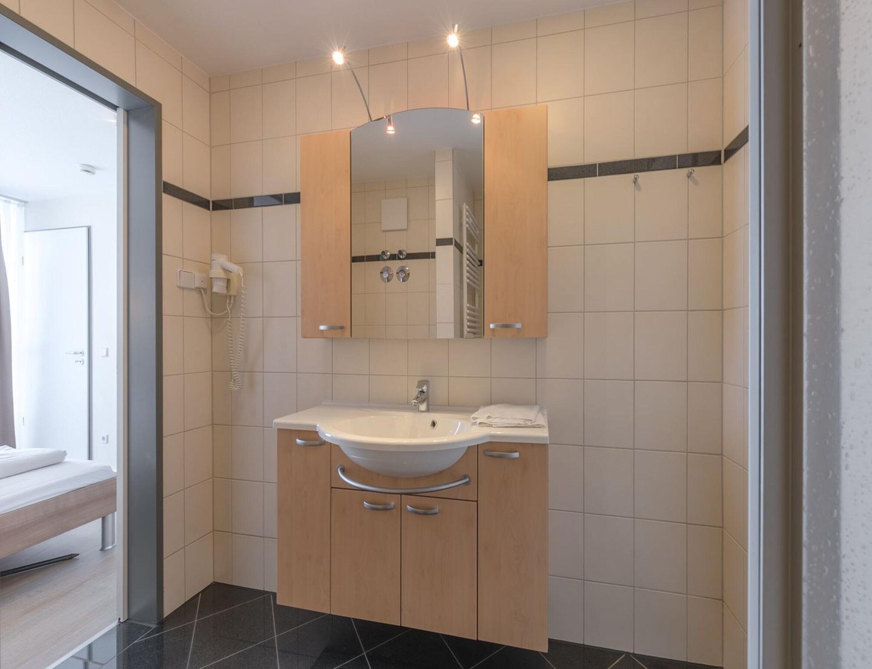 A modern bathroom with a white sink, wooden cabinets, a mirror, and a shower area.