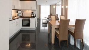 A modern kitchen with white cabinets, a microwave, and a coffee maker. There is a dining area with a wooden table and wicker chairs. - Liebevoll Eingerichtetes Appartement (Rechlin)