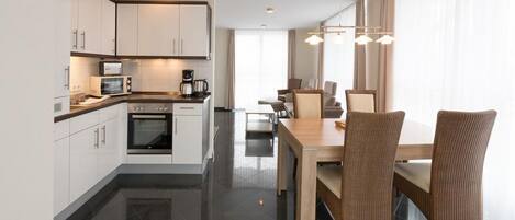 A modern kitchen with white cabinets, a microwave, and a coffee maker. There is a dining area with a wooden table and wicker chairs.