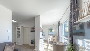 A modern living room with a sofa, a coffee table, and a dining area with chairs. There is a kitchen visible through an open door. - Liebevoll Eingerichtetes Appartement (Rechlin)
