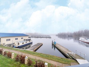 A calm river with a dock and a building with a blue roof. - Liebevoll Eingerichtetes Appartement (Rechlin)