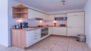 Una cocina compacta con armarios blancos, microondas, estufa y cafetera.