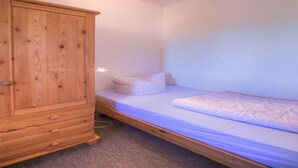 Una habitación pequeña y poco amueblada, con una cama individual, un armario de madera y una luz instalada en la pared.