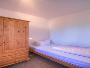 Una stanza piccola e modesta, con un letto singolo, un armadio in legno e una lampada a parete.