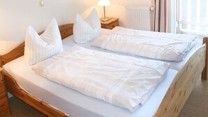 En dobbeltseng med hvide sengetøj og puder, et natbord med lampe, og et vindue med gardiner.