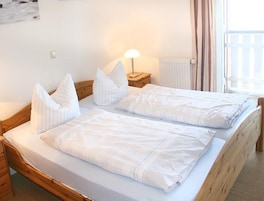 A double bed with white linens and pillows, a bedside table with a lamp, and a window with curtains.