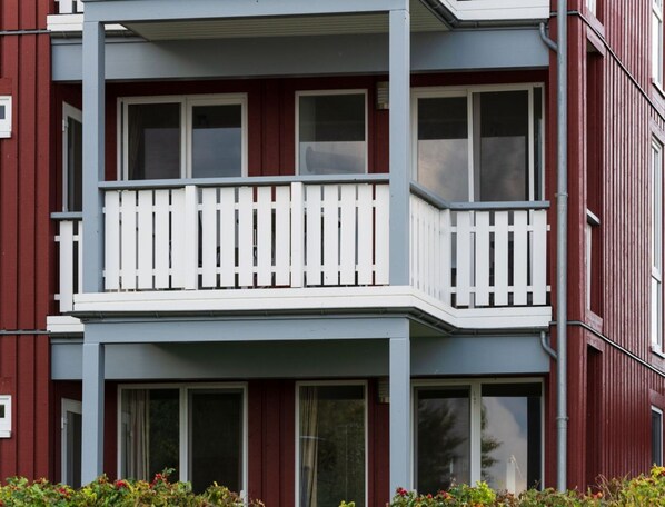 Un edificio residencial de varios pisos con balcones, ventanas amplias y fachada roja.