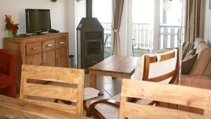 En hyggelig stue med fjernsyn, møbler i træ, en pejs og en balkon med gardiner.