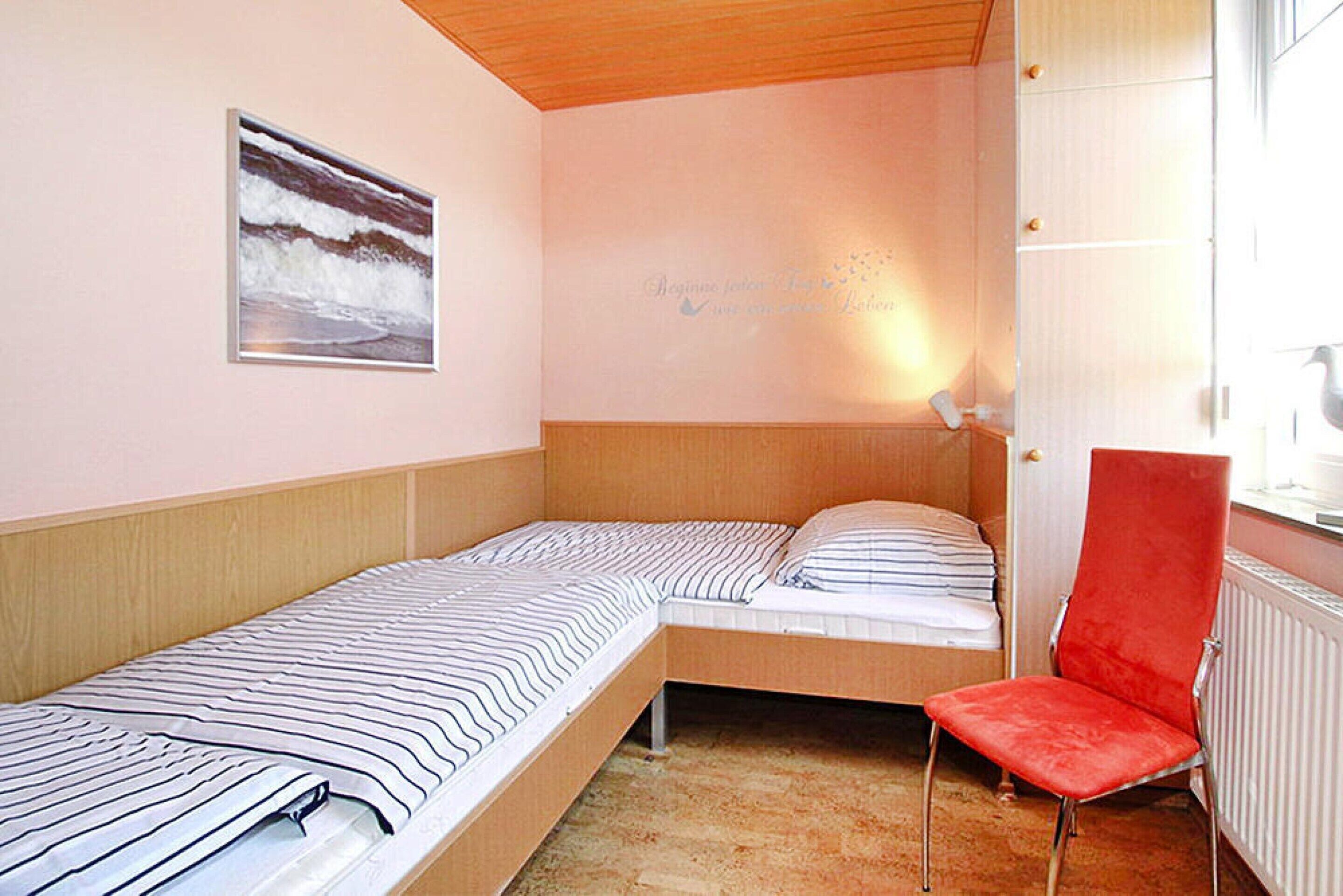 A bedroom with two single beds, a red chair, a painting on the wall, and a window with a view.