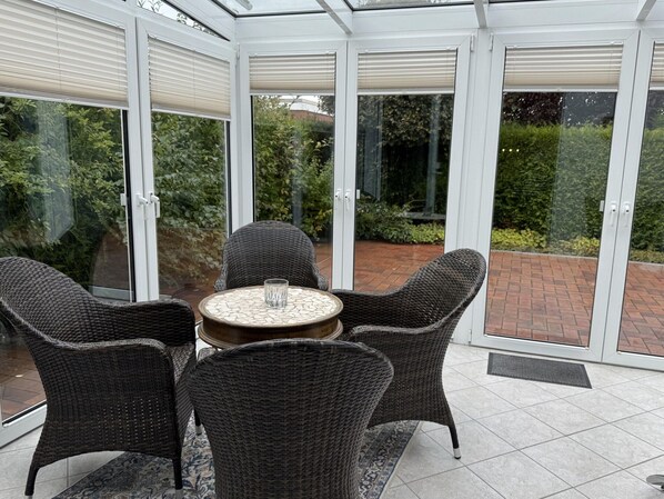 A conservatory with a glass door, wicker furniture, and a tiled floor. - Bungalow, Dornumersiel (Dornum)