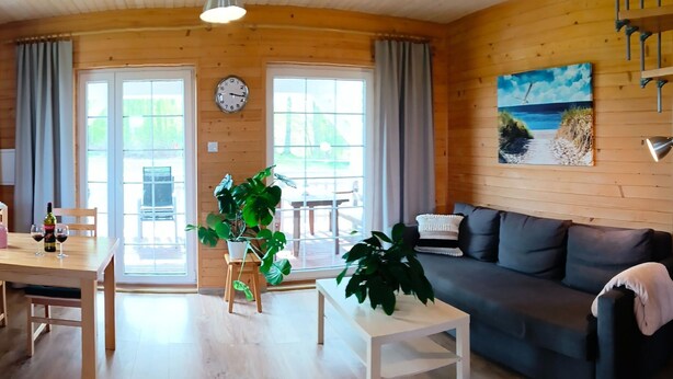 Une pièce chaleureuse avec un décor intérieur en bois, une table à manger avec des chaises, un canapé, une plante en pot et un tableau accroché au mur.