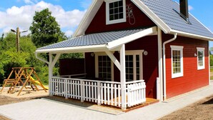 Une maison rouge avec un porche blanc et une cheminée.