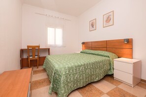 Une chambre à coucher avec un lit, une chaise, une petite table, une table de chevet et une fenêtre.