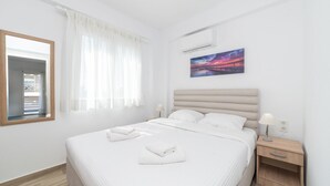 A hotel room with a bed, a nightstand, a lamp, a painting, and a window with sheer curtains. - Amarylis Residential Complex-One Bedroom Apartment (Kavala)