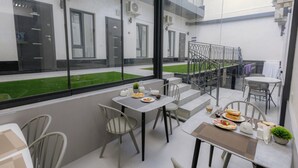 Una zona d'exterior moderna amb taules i caires, un jardí petit i vista a l'exterior de l'edifici.
