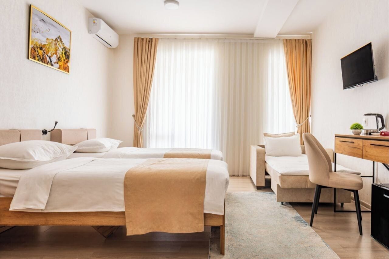 A hotel room with two beds, a desk, a chair, and a TV.