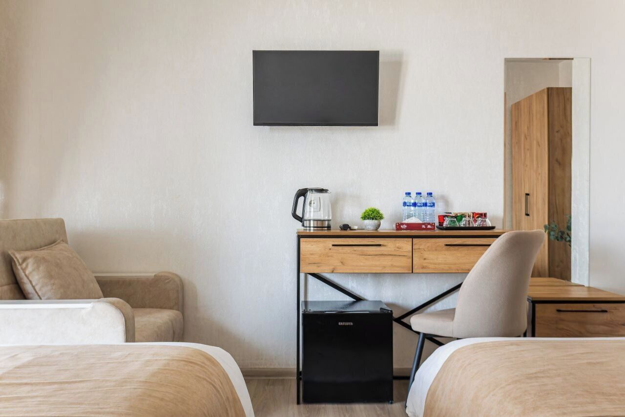 A hotel room with two beds, a desk with a kettle, water bottles, and a TV on the wall.