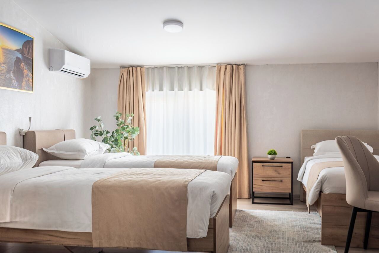 Een hotelkamer met twee bedden, een nachtkastje met lamp, een kleine plant en een raam met gordijnen.